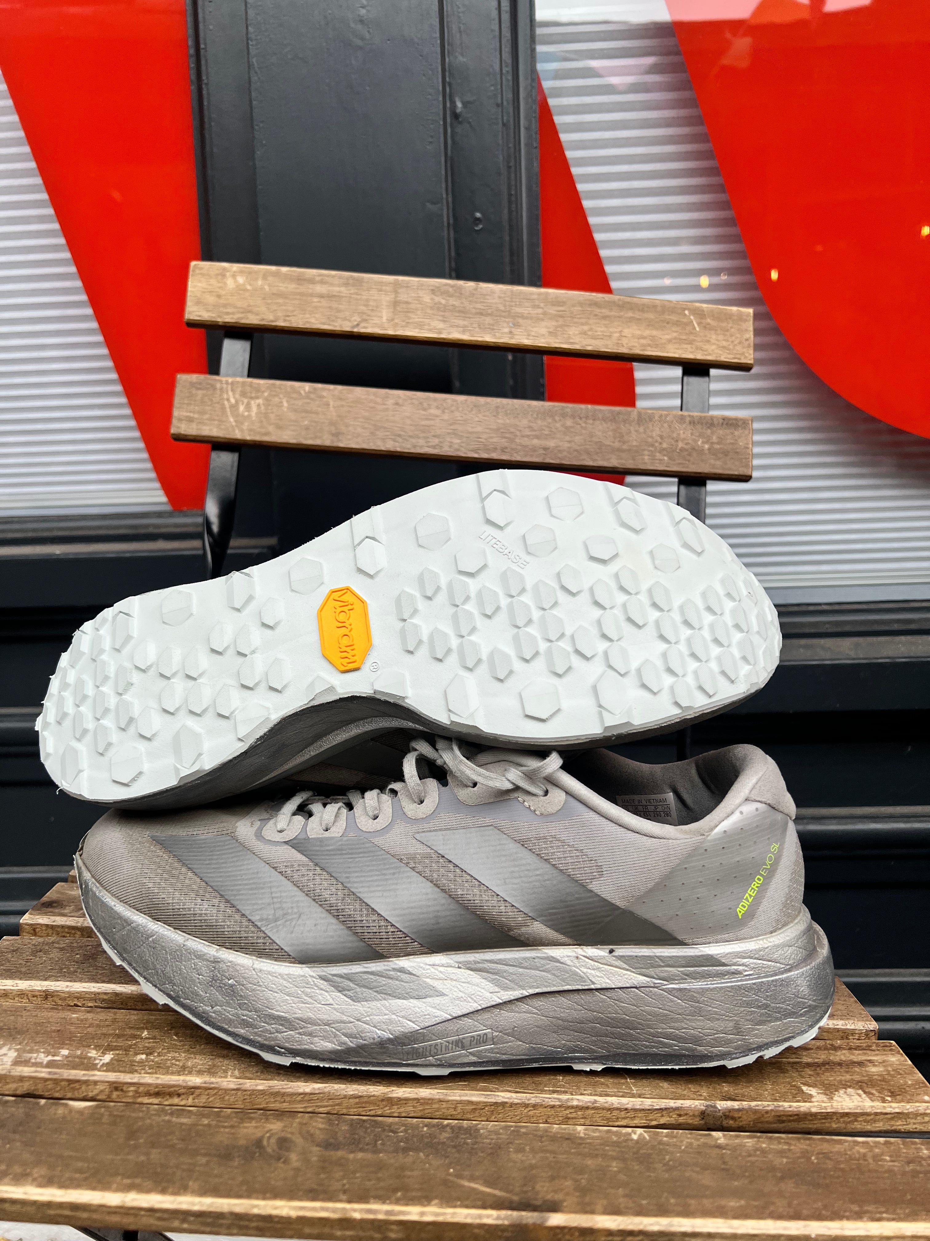 A pair of gray running shoes displayed on a wooden bench, with one shoe flipped to show the white Vibram outsole. Running/Trail Resole - Sole and Trail